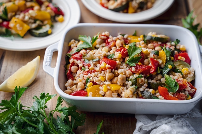 A White Serving Dish is Filled With a Barley Salad that Includes Roasted Vegetables and Fresh Parsley.