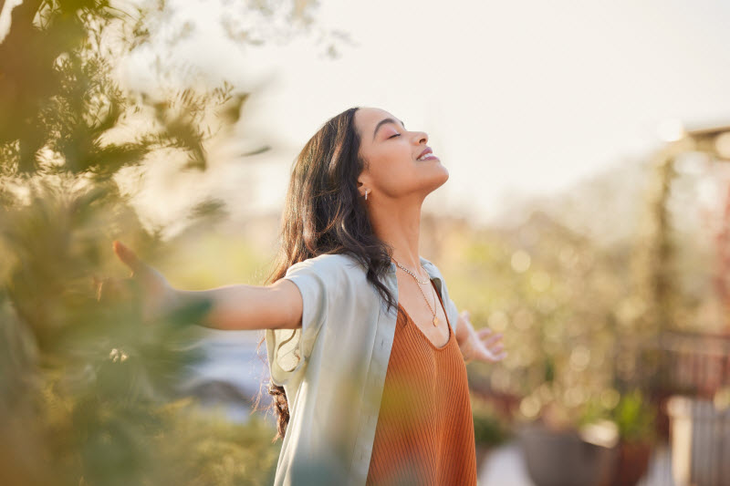 Content-Looking Woman Outdoors With Arms Outstretched and Chin to the Sun to Represent Concept of Health and Wellness Tips