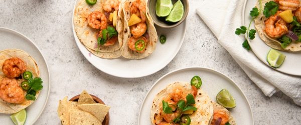 Four Small Plates Have Individual Servings of Grilled Shrimp Tacos With Fresh Lime, Sliced Jalapeno and Cilantro.