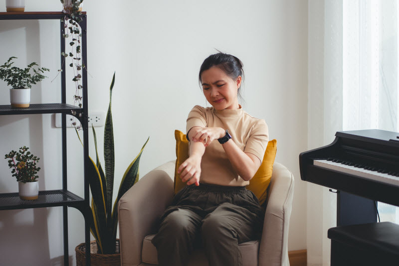 Woman Sitting on Chair in Living Room Skin Picking Arm as She Struggles With Body Focused Repetitive Behavior Disorder
