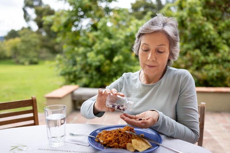 An Older Woman Prepares to Take a Digestive Enzyme Before a Meal.