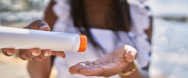 Woman Pouring Sunscreen into Palm of Hand at Beach to Represent Concept Is Sunscreen Bad for You
