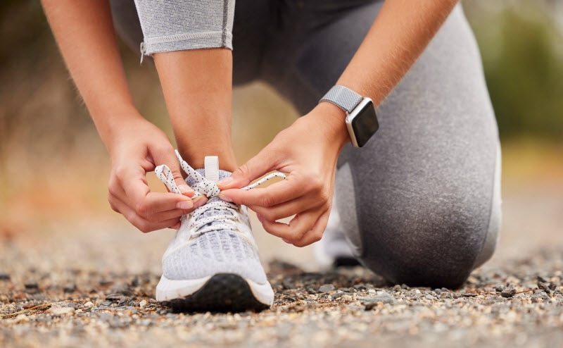 Cropped View of Woman Couched Down Tying Sneaker to Represent Concept of Interval Walking