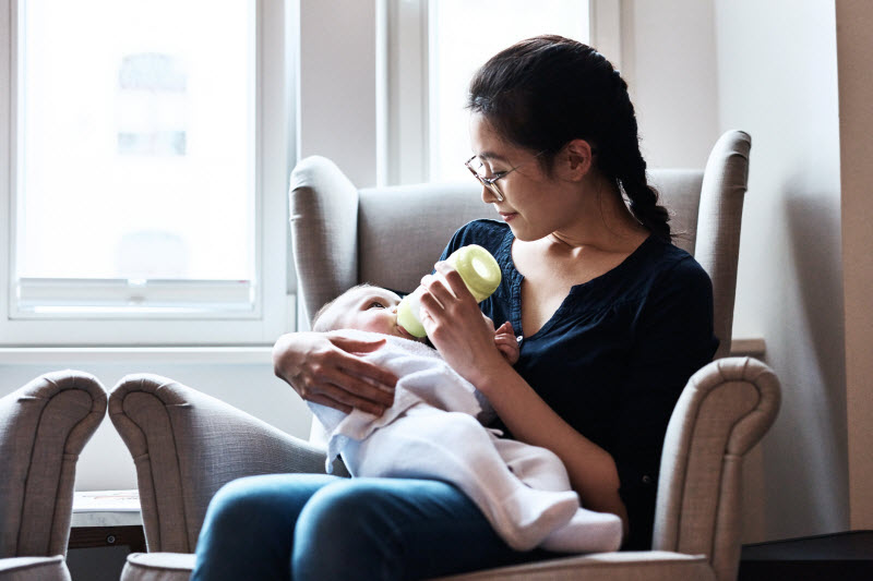 Mother Feeding Baby From Bottle in Cozy Living Room Chair to Represent Concept of Operation Stork Speed Infant Formula Review
