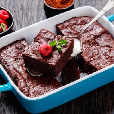 A Blue Baking Dish With Raspberry Brownies is Sliced into Squares With a Small Bowl of Fresh Raspberries on the Side for Garnish.