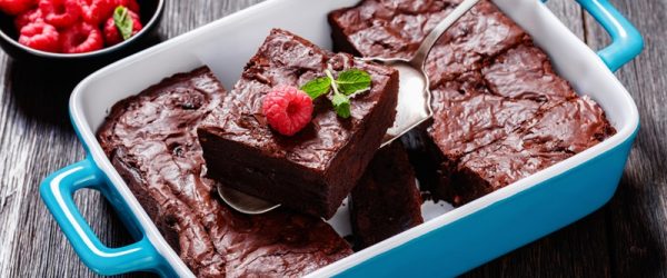 A Blue Baking Dish With Raspberry Brownies is Sliced into Squares With a Small Bowl of Fresh Raspberries on the Side for Garnish.