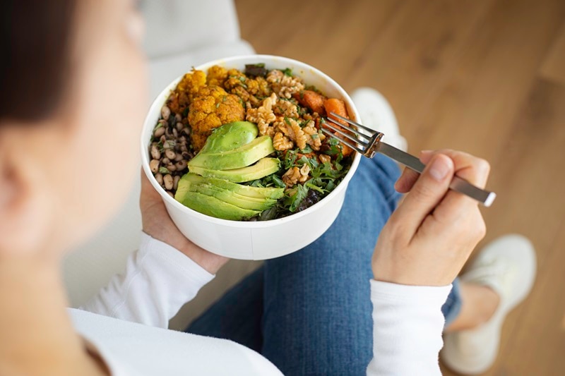 A Woman Eats a Healthy Bowl of Vegetables, Greens and Beans, Representing Signs You're Not Getting Enough Protein.