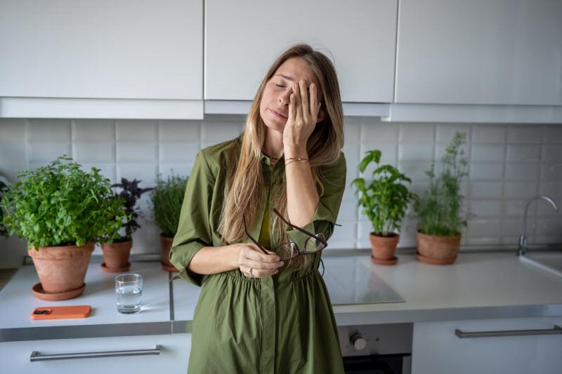 Tired-Looking Woman in Kitchen Rubbing Eyes Thinking She Should Reset With a Brain Detox