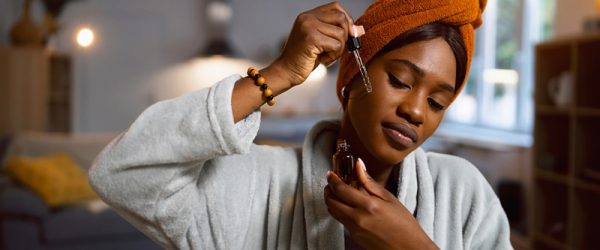 A Young Woman in a Robe Applies a Serum to Her Cheek, Representing Apricot Oil Benefits.