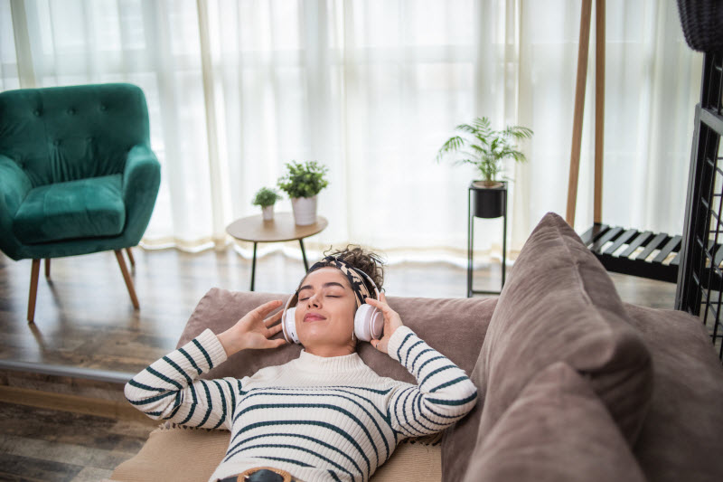 Woman on Couch With Eyes Closed and Headphones on Practicing Cozymaxxing While Learning How to Relax