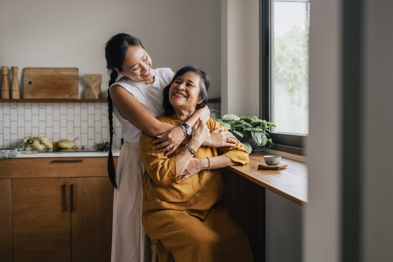 Concept of Mini Stroke Symptoms Represented by Adult Daughter Hugging Mother in Kitchen