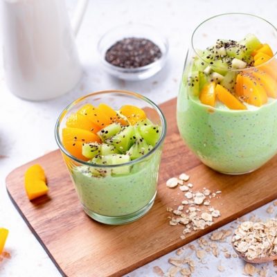 Two Glasses Are Filled With Matcha Overnight Oats and Topped With Sliced Kiwi and Peaches.