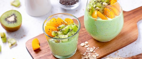 Two Glasses Are Filled With Matcha Overnight Oats and Topped With Sliced Kiwi and Peaches.