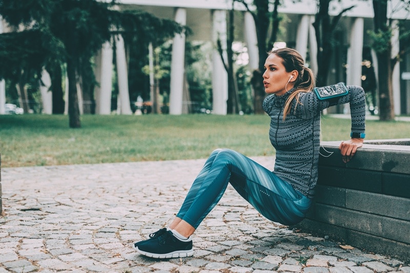 A Young Woman Does Tricep Dips Outdoors, Representing a No-Equipment Arm Workout.
