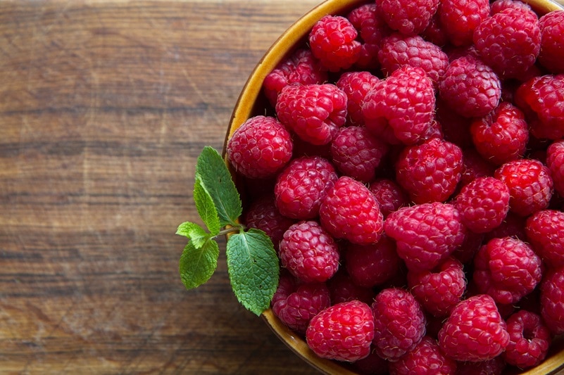 A Bowl is Filled to the Brim With Fresh Raspberries, Topped With a Sprig of Fresh Mint, Representing Raspberry Benefits.