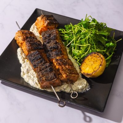 Two Grilled Salmon Skewers Are Served Over a Potato Salad Beside an Herb Green Salad and Half a Grilled Lemon.