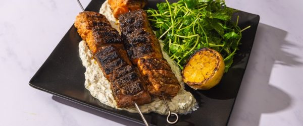 Two Grilled Salmon Skewers Are Served Over a Potato Salad Beside an Herb Green Salad and Half a Grilled Lemon.