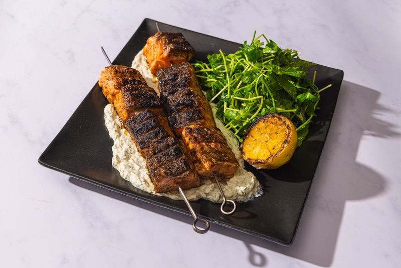 Two Grilled Salmon Skewers Are Served Over a Potato Salad Beside an Herb Green Salad and Half a Grilled Lemon.