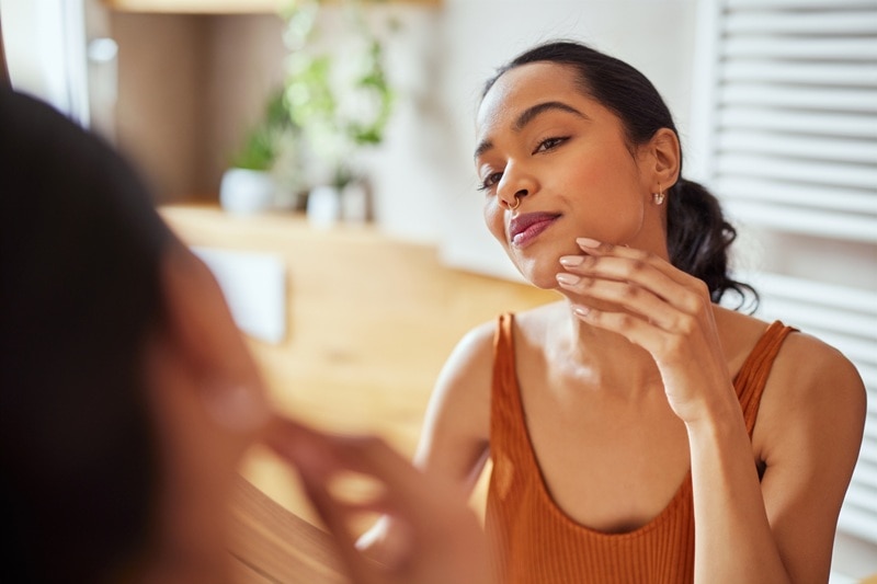 A Woman Checks Her Skin in the Mirror, Representing a Skincare Plateau.