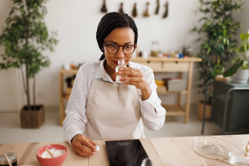 Woman Wearing Glasses Sitting at Desk Sniffing Bottle of Essential Oils for Energy