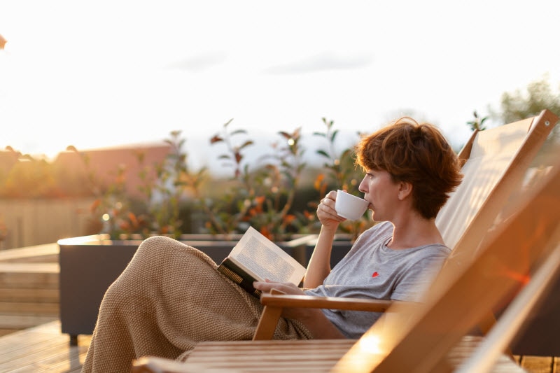 Woman Participating in the No Buy Challenge Relaxing in Deck Chair Reading Book and Sipping Coffee