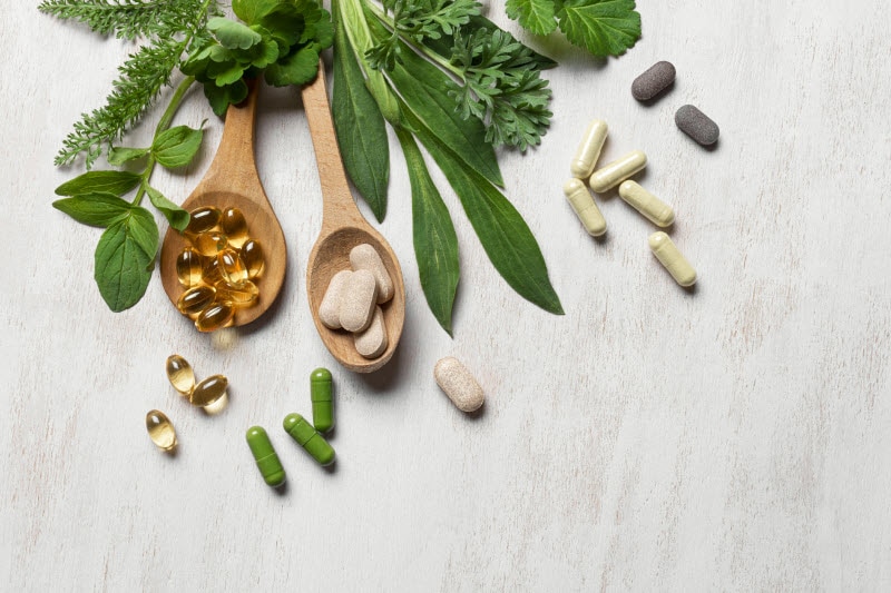 Overhead View of Various Supplements Scattered and On Wooden Spoons with Greenery to Represent Concept of Vitamin Recalls