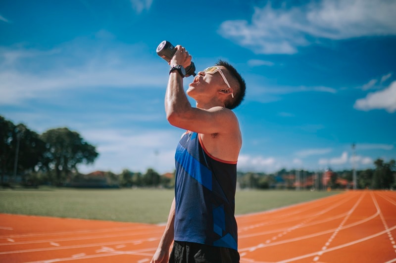 A Fit Man Takes a Break from Running on an Outdoor Track and Drinks from a Bottle, Representing What Happens When Your Body is Low on Electrolytes.