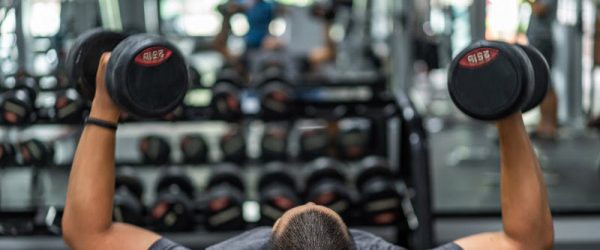 Concept of What is Bigorexia Represented by Muscular Man Lifting Weights While Lying on Bench at Gym