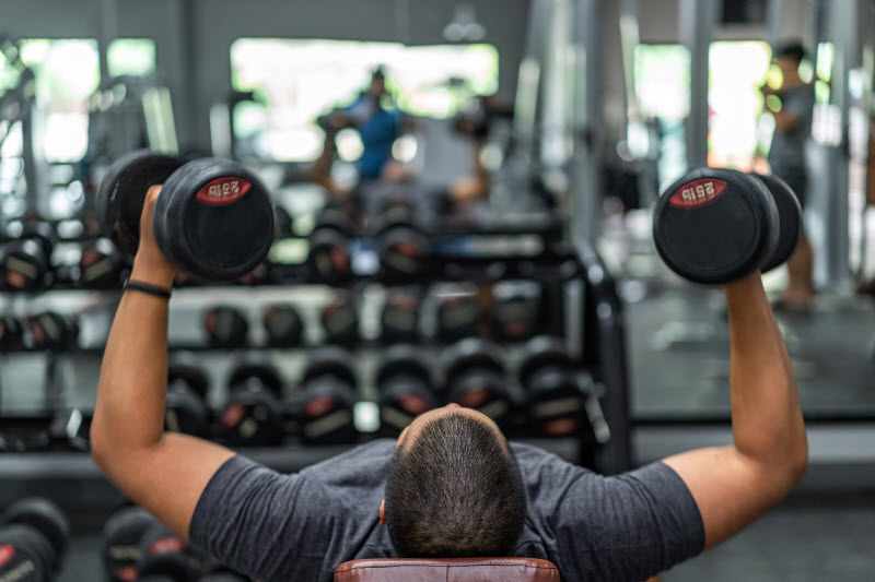 Concept of What is Bigorexia Represented by Muscular Man Lifting Weights While Lying on Bench at Gym
