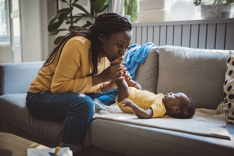 A Mother Happily Kisses Her Newborn Baby's Feet in a Home Setting, Representing the Question, "What is Postpartum Depression?"