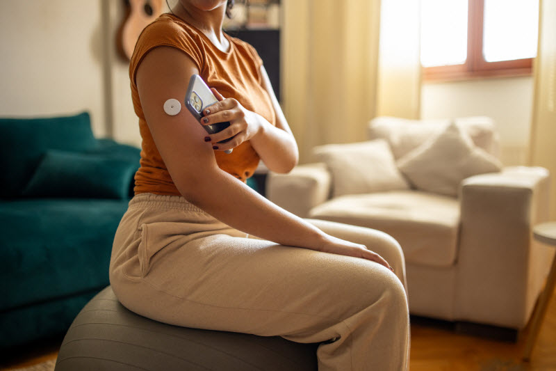 Woman Taking Glucose Reading on Couch Wondering Why is My Blood Sugar High in the Morning