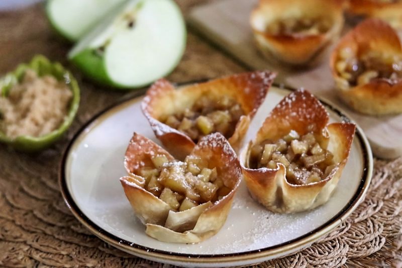 Powdered Sugar-Dusted, Browned Wonton Cups Filled with Cinnamon Apple Bits on a Dessert Plate Surrounded by Slices of Granny Smith Apples