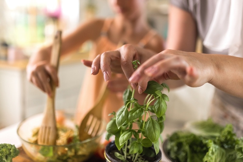A Woman Tears a Sprig of Basil from a Plant While Working in the Kitchen to Make a Salad, Representing Basil Benefits.