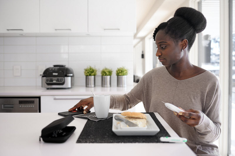 Woman Testing for Elevated Blood Sugar Sitting on Stool at Counter in Minimalist Kitchen