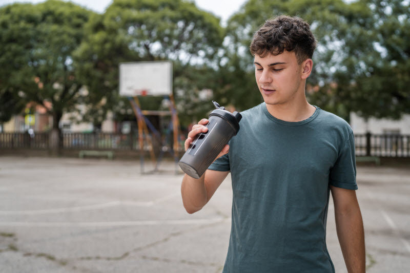 Concept of Is Protein Powder Safe for Teens Represented by Teenage Boy Drinking Protein Shake on Outdoor Basketball Court