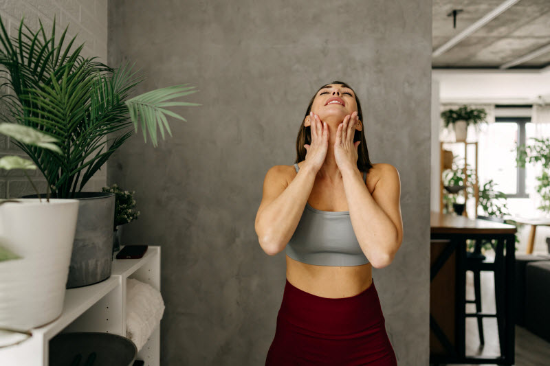 Woman in Workout Clothing Doing Lymphatic Drainage Massage on Herself in Modern Living Room Setting