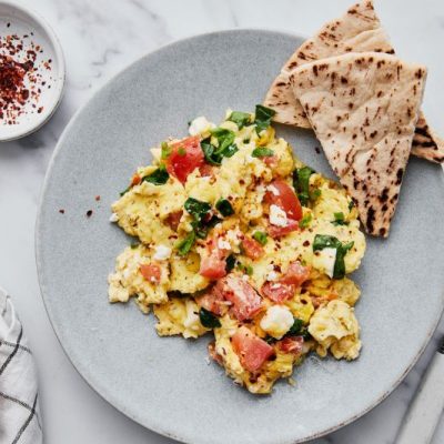 Greek Yogurt Eggs Scrambled with Tomato, Spinach and Feta Cheese on an Earthenware Plate with Pita Bread and Greek Olives