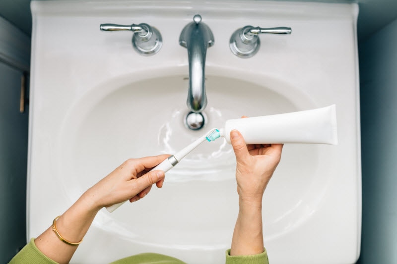 Overhead View of Woman's Hands Over Sink Applying Toothpaste to Toothbrush to Represent Concept of Menopause and Oral Health