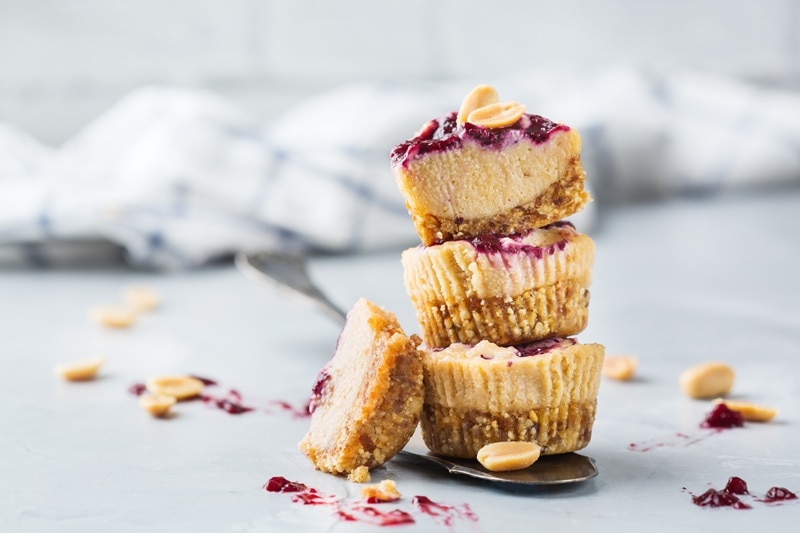 Three Peanut Butter and Jelly Cheesecake Bites are Stacked on Top of One Another, Showing Bits of Beautiful, Purple Jam on Top.