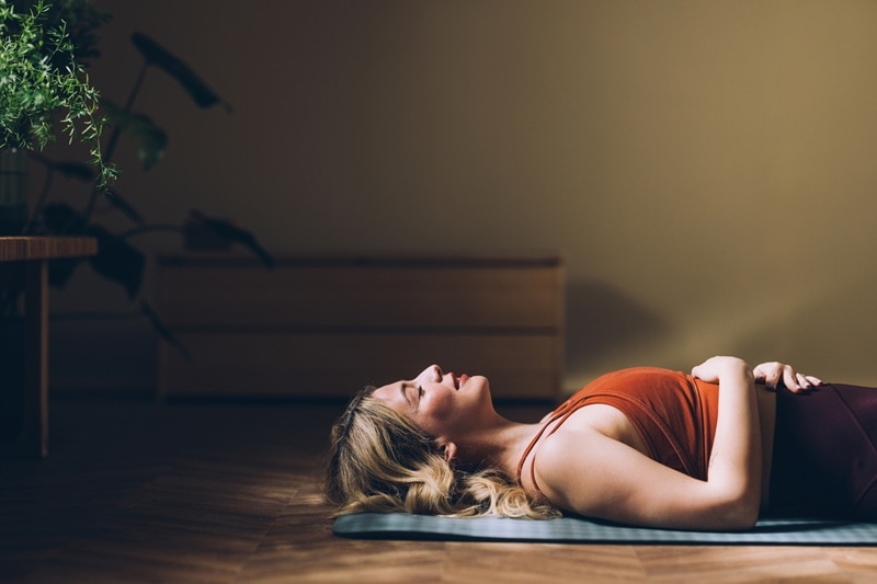 A Woman Lies On Her Back With Her Eyes Closed, Practicing Pelvic Floor Relaxation Exercises