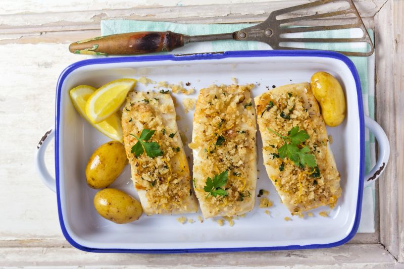 Baked Cod Dotted with Oregano Leaves in Enamel Baking Dish with Fingerling Potatoes and Lemon Wedges