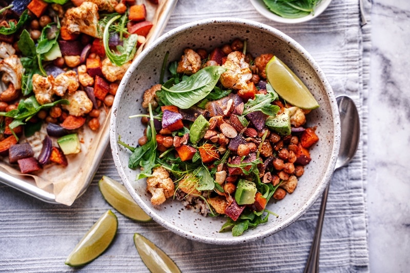 A Sweet Potato Sheet Pan Dinner Includes Roasted Chickpeas, Cauliflower and Red Onions and is Topped With Fresh Basil, Avocado and a Wedge of Lime.