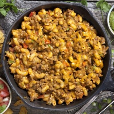 Overhead Shot of Taco Macaroni and Cheese Loaded with Cheese-Covered Ground Beef in a Cast Iron Skillet Surrounded by Fresh Salsa & Guacamole