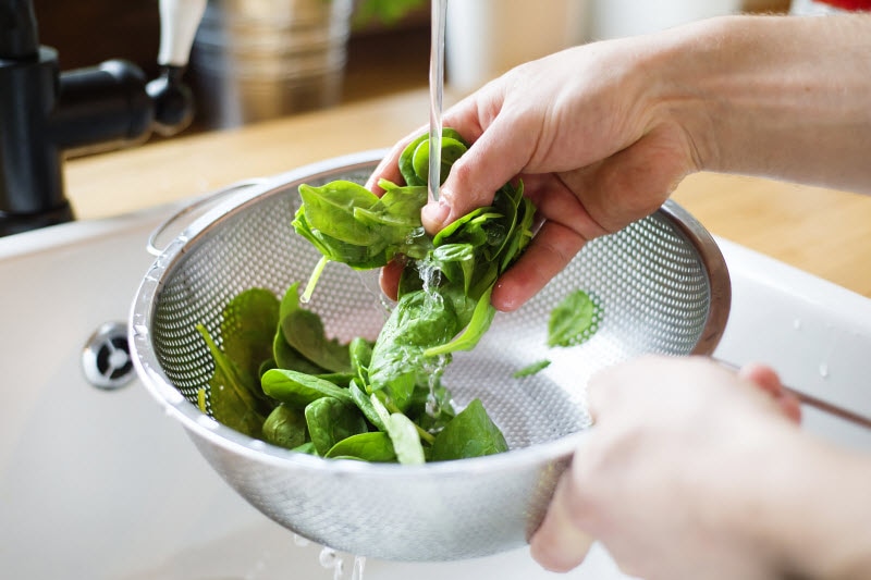 Person Washing Leafy Greens in Colander Over Sink to Represent Concept of Food Mold and Mycotoxins