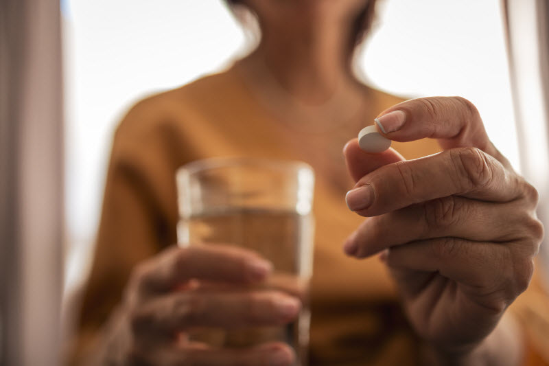 Concept of Red Flags in Dietary Supplements Represented by Closeup View of Woman Holding Tablet and Glass of Water