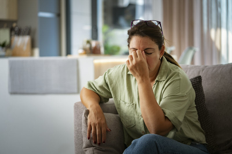 Woman Trying to Use Acupressure Points for Head Pain Relief While Sitting on Couch in Living Room