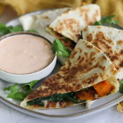 Four Wedges of a Butternut Squash, Spinach & Cheese Quesadilla on Plate with Parsley and a Shallow, Round Bowl of Chipotle Cream Sauce