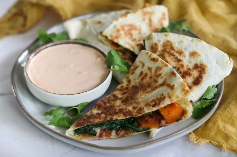 Four Wedges of a Butternut Squash, Spinach & Cheese Quesadilla on Plate with Parsley and a Shallow, Round Bowl of Chipotle Cream Sauce