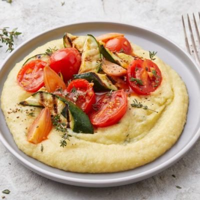 On a Plate, a Circle of Creamy Polenta is Generously Topped With Roasted Veggies. A Fork Waits Nearby