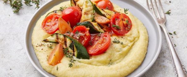 On a Plate, a Circle of Creamy Polenta is Generously Topped With Roasted Veggies. A Fork Waits Nearby
